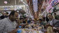 Umat muslim berkumpul di meja sepanjang jalan untuk berbuka puasa bersama dalam jamuan buka puasa massal pada hari ke-15 bulan suci Ramadhan di pinggiran Matariya, timur laut Kairo, Mesir, 16 April 2022. (Khaled DESOUKI/AFP)