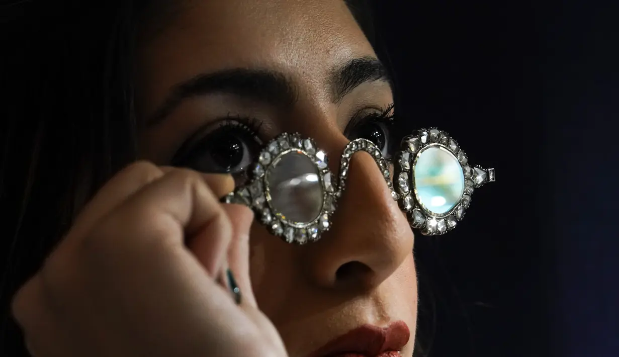 Seorang anggota staf mengenakan kacamata Mughal dengan lensa berlian, dalam bingkai berlian, di Sotheby's, di London, Jumat (22/10/2021). Dua pasang kacamata dari abad ke-17 ini akan dilelang 27 Oktober dengan perkiraan £1,5-2,5 Juta atau. (AP Photo/Alberto Pezzali)