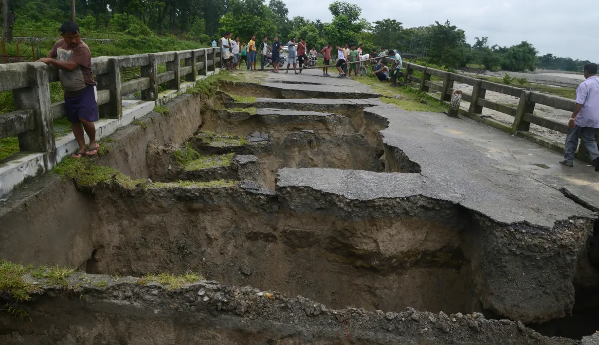 Warga India berkumpul melihat sebuah jembatan yang hancur akibat hujan deras di Desa Toribari, pinggiran Siliguri, Kamis (21/7). Hujan deras yang terus menerus turun di India dalam 48 jam terakhir menyebabkan banjir dan tanah longsor. (DIPTENDU Dutta/AFP)