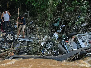 Orang-orang mencoba menyelamatkan barang-barang dari mobil yang hancur akibat banjir bandang di Petropolis, Brasil, 16 Februari 2022. Sebanyak 55 orang tewas dalam banjir bandang dan tanah longsor yang menghancurkan Kota Petropolis. (CARL DE SOUZA/AFP)