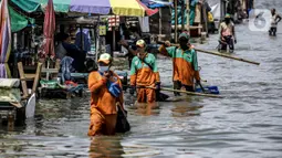 Petugas PPSU membersihkan sampah saat terjadi banjir rob di Pelabuhan Kali Adem, Muara Angke, Jakarta, Selasa (9/11/2021). Walau terendam banjir rob, petugas PPSU tetap sigap bersihkan sampah yang mengambang terbawa air laut. (Liputan6.com/Faizal Fanani)