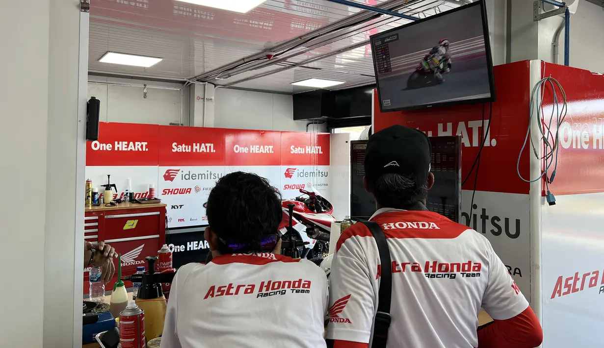 Dua orang mekanik Astra Honda Racing Team (AHRT) menyaksikan rekaman balapan dari televisi di sela mempersiapkan motor pembalapnya yang akan bertarung di balapan hari kedua ARRC Mandalika 2023 di Sirkuit Mandalika, Lombok, Sabtu (12/8/2023). (Bola.com/Iqri Widya)