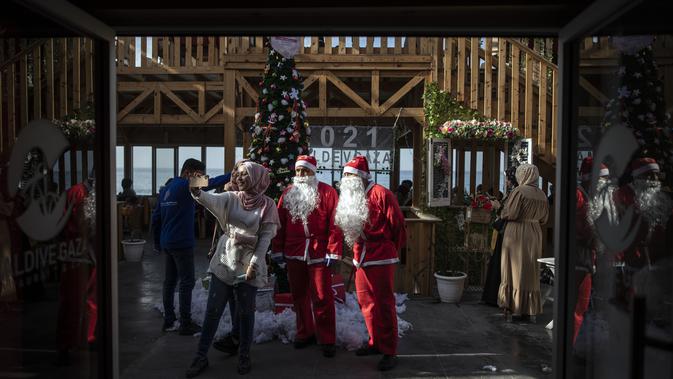 Warga Palestina berswafoto dengan pramusaji yang berpakaian Sinterklas di sebuah restoran di pantai di Kota Gaza, Minggu (13/12/2020). Restoran tersebut didandani dengan tema Natal, pelayanannya pun berpakaian seperti Sinterklas. (AP Photo/Khalil Hamra)