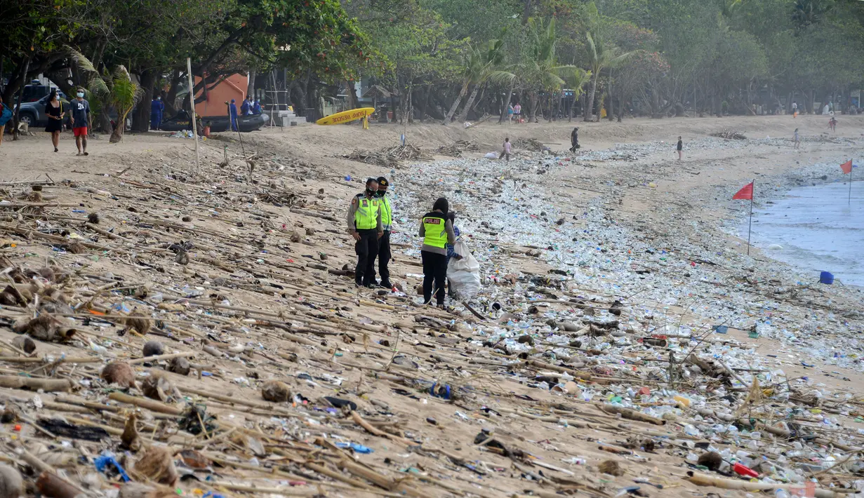 Polisi berdiri di antara sampah kiriman yang terdampar memenuhi pesisir pantai Kuta, Bali, Kamis (31/12/2020). Menjelang pergantian tahun baru, Pantai Kuta hanya terlihat beberapa wisatawan, namun tumpukan sampah kiriman tersebar di sepanjang bibir pantai. (SONNY TUMBELAKA / AFP)
