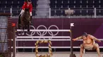 Atlet berkuda Kanada Mario Deslauriers mengendarai Bardolina 2 melewati patung pesumo dalam kualifikasi individu lompat berkuda Olimpiade Tokyo 2020 di Equestrian Park di Tokyo (3/8/2021). Pihak panitia memasang patung simbol Jepang seperti sakura sampai pesumo di arena lintasan. (AFP/Behrouz Mehri)