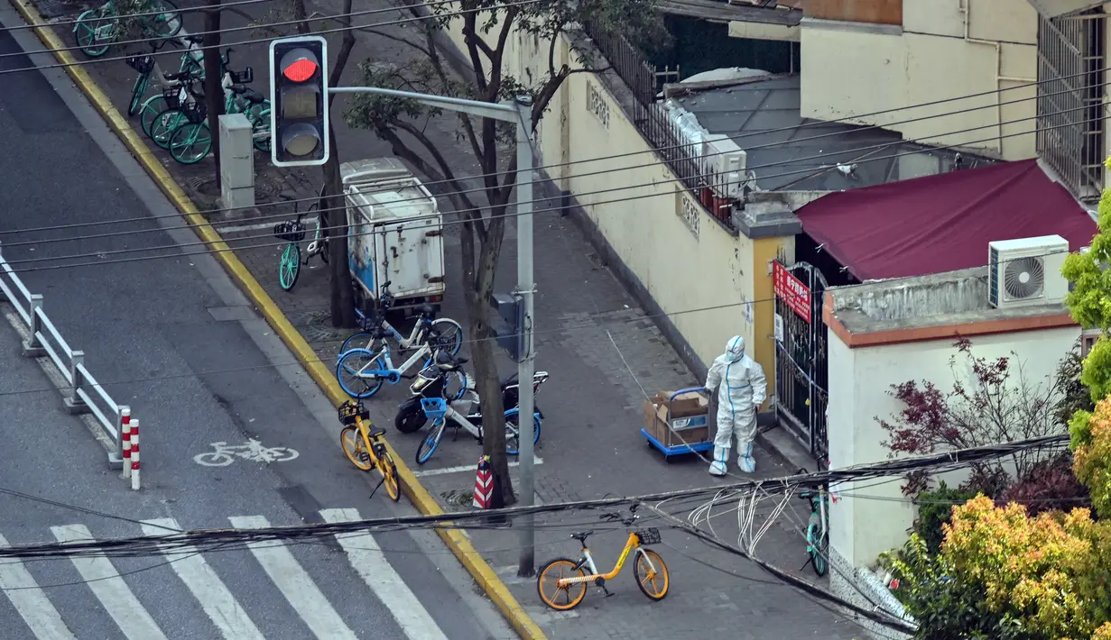 Seorang pekerja yang mengenakan alat pelindung diri berdiri di sebelah pintu masuk ke lingkungan saat lockdown tahap kedua akibat COVID-19 di Distrik Jing'an, Shanghai, China, Rabu (6/4/2022). (Hector RETAMAL/AFP)