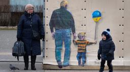 Orang-orang melewati karya seni dari seniman jalanan terkenal TvBoy yang dibuat pada dinding di Kota Bucha, Ukraina, 30 Januari 2023. Karya seni yang dibuat untuk menghormati para korban perang Rusia-Ukraina tersebut mengandung pesan kelahiran kembali dan harapan serta berharap agar konflik segera berakhir. (AP Photo/Efrem Lukatsky)