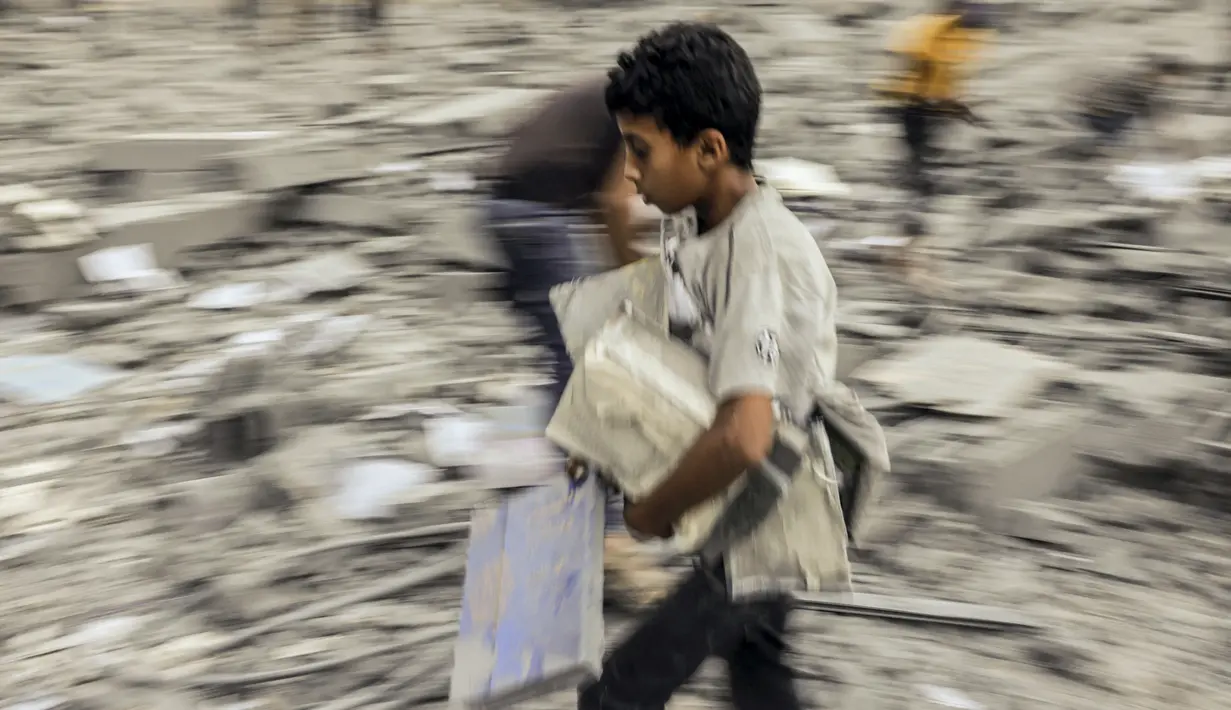 Seorang anak berjalan pergi dengan barang-barang yang diselamatkan dari reruntuhan bangunan yang terkena serangan Israel di Rafah di Jalur Gaza selatan pada 15 Oktober 2023. (Photo by MOHAMMED ABED / AFP)