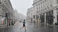 Warga yang sedang olahraga harian melintasi Regent Street di London di tengah salju saat ibu kota Inggris mengalami hujan salju yang jarang terjadi pada Minggu (24/1/2021). Hujan salju langka itu membawa kegembiraan di tengah penguncian atau penutupan wilayah (lockdown) nasional (JUSTIN TALLIS/AFP)