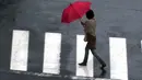 Seorang wanita menyeberang jalan di tengah hujan dari Topan Mindulle di Tokyo, Jepang, Jumat (1/10/2021). Topan Mindulle sedang bergerak di lepas pantai Jepang. (AP Photo/Eugene Hoshiko)
