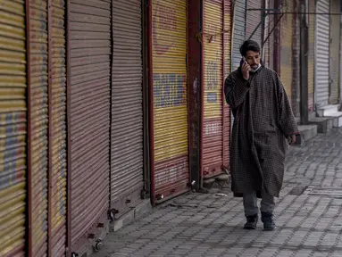 Pria Kashmir berjalan di luar pasar tertutup di Srinagar, Kashmir yang dikuasai India, Sabtu (15/1/2022). Pihak berwenang di bagian Kashmir India mengumumkan pembatasan penuh pergerakan yang tidak penting selama akhir pekan di seluruh negara bagian untuk mengekang COVID-19. (AP Photo/Dar Yasin)