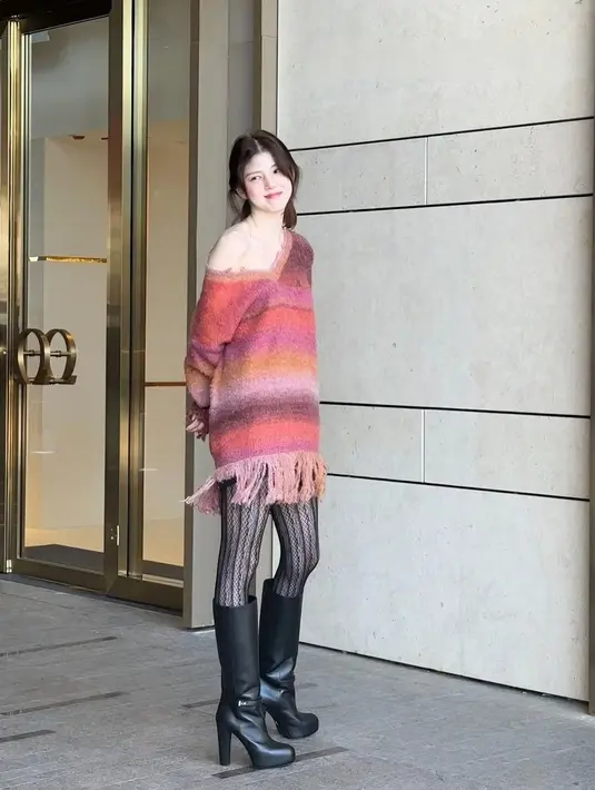 Han So Hee terlihat mengenakan boho sweater dress bernuansa merah muda dengan bahu yang dibuat asimetris menampilkan kulitnya yang putih. Ia memadukan penampilannya yang unik dengan stoking jaring dan high boots berwarna hitam. [Foto: Instagram/xeesoxee_luv]