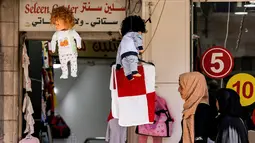 Wanita Palestina berjalan melewati boneka di luar toko pakaian bayi di pasar di kota tua Betlehem di Tepi Barat yang diduduki (14/9/2021).  Ekonomi Palestina diperkirakan akan tumbuh empat persen pada tahun 2021 setelah terpukul pada tahun 2020 akibat pandemi COVID-19. (AFP/Emmanuel Dunand)