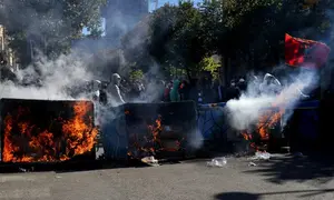 Sejumlah demonstran berdiri di belakang tempat sampah yang terbakar saat aksi unjuk rasa antipemerintah di depan gedung Kementerian Pendidikan di Tirana, Albania, Sabtu (17/10/2026). (Dok. AP Photo/Hameraldi Agolli)