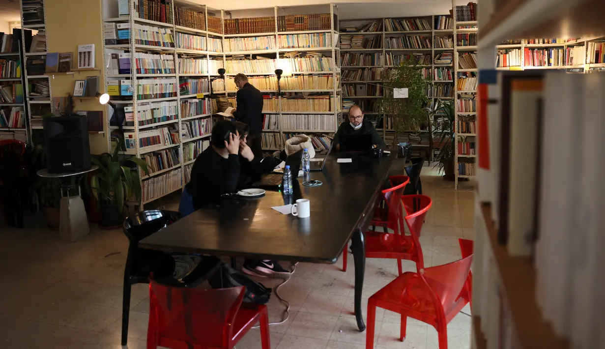 Orang-orang Lebanon duduk dengan laptop mereka di sebuah kafe di Beirut pada 14 Januari 2022.	Kafe-kafe Beirut sekarang berfungsi sebagai tempat kerja pengganti bagi orang-orang yang bergulat dengan kekurangan listrik dan pemutusan internet yang berasal dari krisis ekonomi. (JOSEPH EID / AFP)