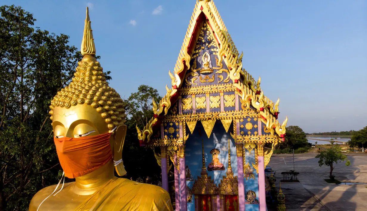 Sebuah foto udara menunjukkan masker diletakkan pada wajah patung Buddha raksasa di kuil Wat Nithet Rat Pradit di Pathum Thani di luar Bangkok, Thailand, 12 Mei 2020. Pemasangan masker tersebut sebagai tanggapan terhadap penyebaran pandemi Covid-19. (Photo by Mladen ANTONOV / AFP)