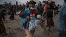 Seorang warga membawa seorang anak ketika orang-orang menyelamatkan barang-barang mereka di daerah yang tertutup abu vulkanik setelah letusan gunung berapi Semeru di desa Sumber Wuluh di Lumajang, Jawa Timur, Minggu (5/12/2021). (AFP /Juni Kriswanto)