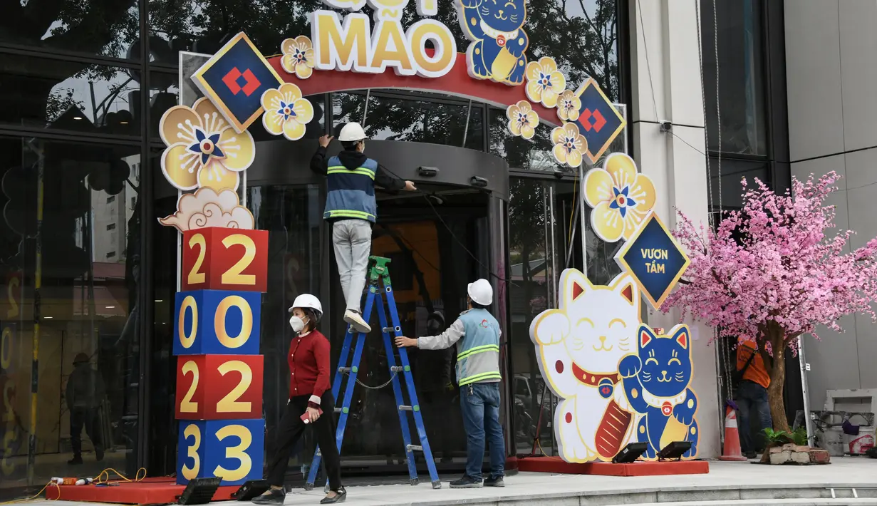 <p>Foto pada 16 Januari 2023 ini menunjukkan para pekerja mendekorasi patung kucing di pintu masuk gedung di Hanoi, menjelang tahun baru Imlek. Bagi kebanyakan orang Vietnam, kucing adalah teman keluarga yang membantu melindungi tanaman dan makanan dari hewan pengerat, sekaligus dipercaya bisa mengusir roh jahat dan membawa keberuntungan. (Nhac NGUYEN / AFP)</p>