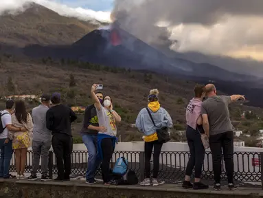 Wisatawan melihat dan berswafoto dengan latar gunung berapi yang meletus di Canary, Pulau La Palma, Spanyol, 26 Oktober 2021. Para pejabat mengatakan gunung berapi yang meletus selama lima minggu terakhir di Pulau La Palma lebih aktif dari sebelumnya. (AP Photo/Emilio Morenatti)