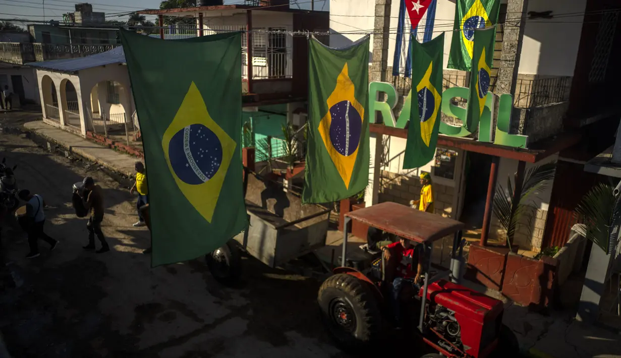 Bendera Brasil digantung di atas traktor yang menarik trailer penggemar sepak bola dan musisi ke rumah Alberto Izquierdo, presiden asosiasi penggemar tim Brasil, untuk menonton pertandingan Grup G Piala Dunia 2022 antara Brasil vs Swiss  di Bauta, Kuba, Senin (28/11/2022). Orang-orang di kotamadya Bauta telah berkumpul untuk mendukung tim Brasil di setiap Piala Dunia selama 20 tahun terakhir. (AP Photo/Ramon Espinosa)