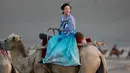 Seorang wanita mengenakan pakaian tradisional menaiki unta di padang pasir di Dunhuang di provinsi Gansu di China barat laut (10/8/2019). Sensus Tiongkok 2000 melaporkan bahwa terdapat 187,578 penduduk di kota tersebut. (AFP Photo/Str)