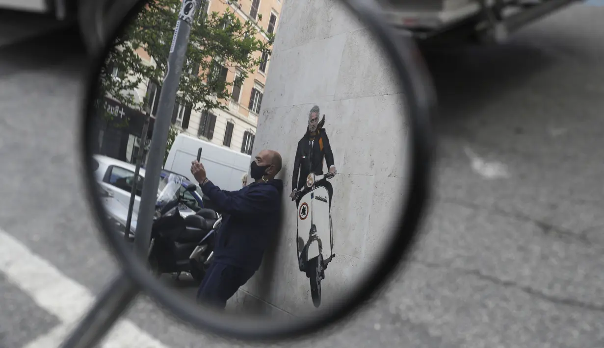 Seorang pria berselfie di dekat mural pelatih Jose Mourinho mengendarai skuter Vespa berhias lambang AS Roma di lingkungan Testaccio,  Roma (7/5/2021). Mourinho cuma 17 bulan menjabat sebagai manajer Tottenham Hotspur. (AP Photo/Gregorio Borgia)
