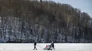 Sebuah keluarga berjalan di danau beku yang tertutup salju dekat Vilnius, Lithuania, Minggu (13/2/2022). Suhu udara 0 derajat Celcius (32 derajat Fahrenheit). (AP Photo/Mindaugas Kulbis)