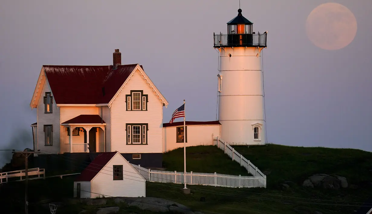 Bulan purnama hampir penuh terlihat dekat Nubble Light di York, Maine, Amerika Serikat, 13 Juni 2022. Fenomena ini disebut juga sebagai Strawberry Supermoon karena terjadi pada saat panen strawberry. (AP Photo/Julio Cortez)