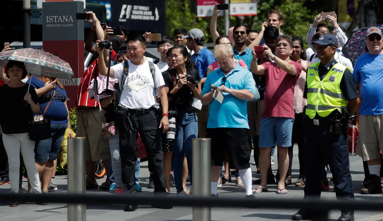 Kerumunan orang melihat iring-iringan mobil Presiden AS, Donald Trump melintasi Orchard Road menuju kediaman resmi PM Lee Hsien Loong di Istana Singapura, Senin (11/6). Trump berkendara menggunakan limosin berbendera Stars and Stripes. (AP/Joseph Nair)