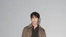 Seung Ju Han mengenakan trench coat cokelat dengan kerah bermotif kotak-kotak khas Burberry, dipadukan sweater rajut gelap, celana plaid gelap, dan boots suede cokelat. [dok. Burberry]