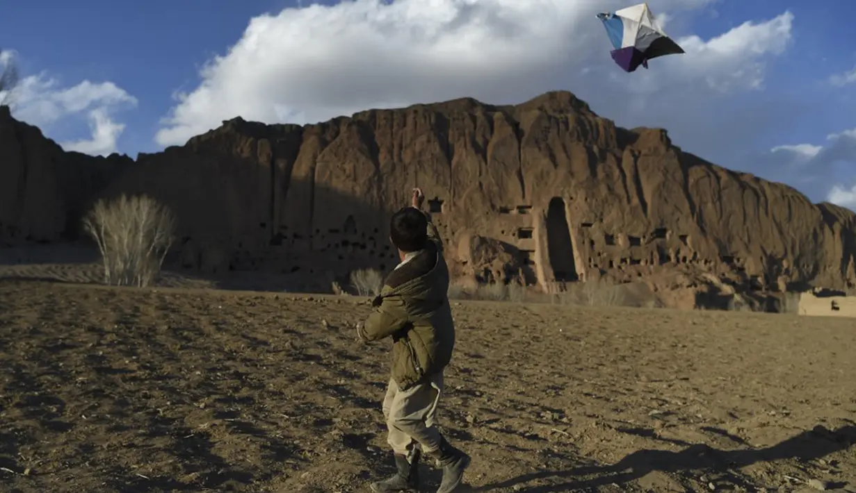 Seorang bocah Hazara menerbangkan layang-layang dekat situs patung Buddha raksasa yang dihancurkan oleh Taliban pada 2001 di Provinsi Bamiyan, Afghanistan, 3 Maret 2021. Pada abad ke-2 hingga invasi Islam abad ke-7, daerah patung ini berdiri menjadi pusat Buddhis yang berkembang. (WAKIL KOHSAR/AFP)