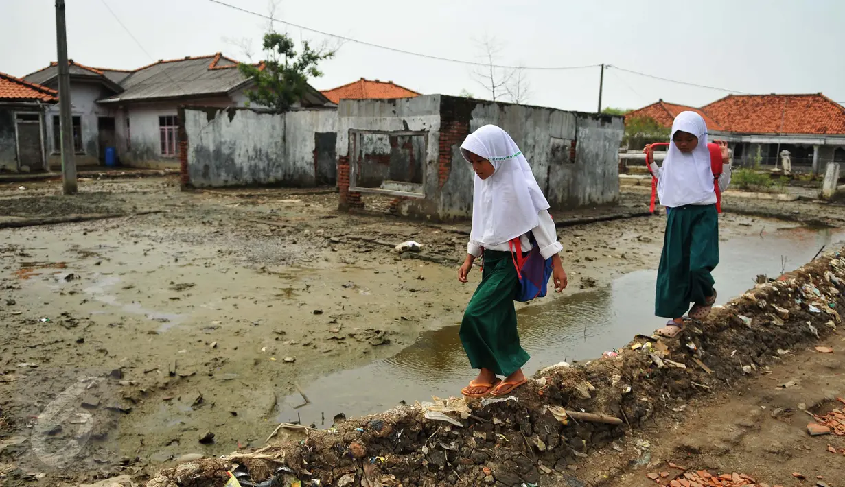 Dua orang siswi melewati pelataran bekas rumah yang terkena dampak abrasi di pantai Muara Gembong, Bekasi, Selasa, (26/7). Tingkat abrasi yang tinggi menyebabkan sejumlah rumah terkikis dan beberapa sekolah terendam air laut. (Liputan6.com/Gempur M Surya)