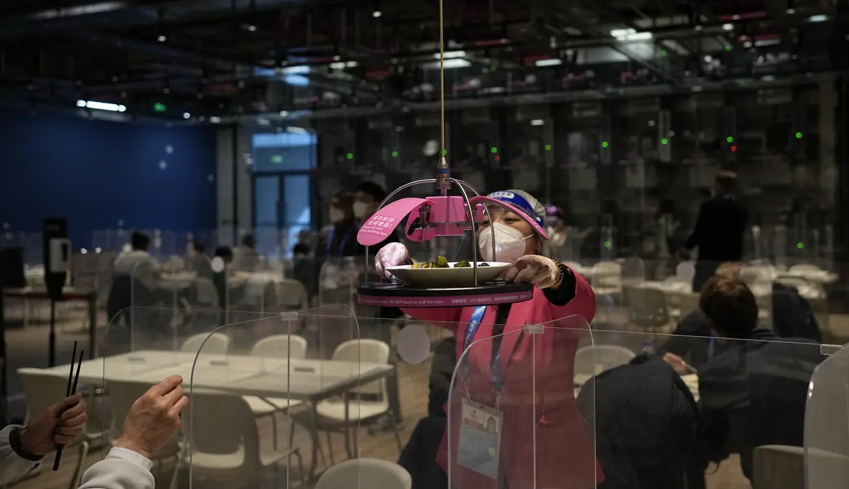Seorang pekerja mengambil makanan yang dikirim ke meja secara robotik di ruang makan media di pusat media utama menjelang Olimpiade Musim Dingin 2022 di Beijing, Rabu (2/2/2022). (AP Photo/Jae C. Hong)
