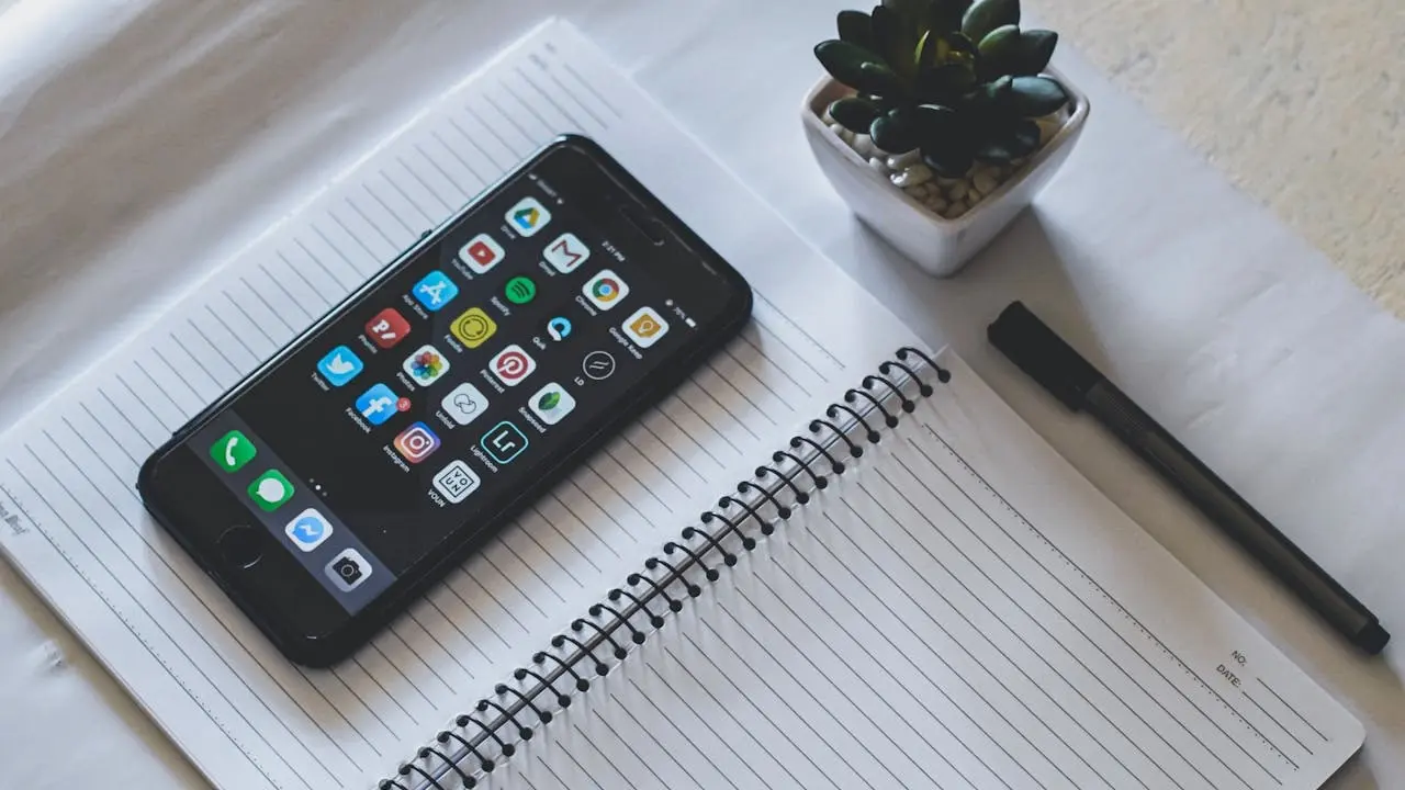 Membuka hp di atas buku (pexels)