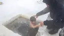 Seorang pria membantu anaknya untuk mandi di air es di Sungai Lena selama perayaan Epiphany tradisional saat suhu turun hingga sekitar -56 derajat di luar Yakutsk, Rusia (19/1/2021). Ritual ini dianggap sebagai salah satu cara untuk para umat Kristen Ortodoks. (AP Photo/Tatiana Gasich)