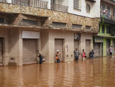 Orang-orang berjalan di jalan yang banjir di Raposos, negara bagian Minas Gerais, Brasil, Selasa (11/1/2022). Tanah longsor akibat hujan deras telah menewaskan sedikitnya 12 orang dan pihak berwenang sedang memantau bendungan yang bisa jebol. (AP Photo/Eugenio Savio)