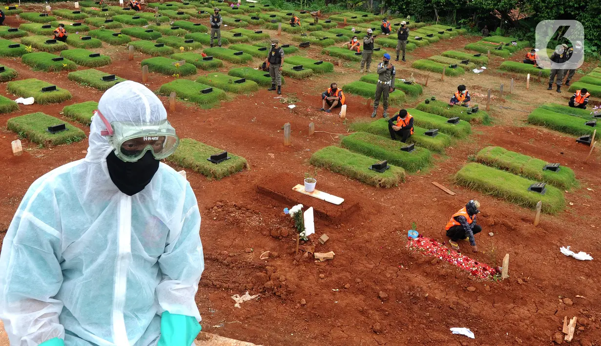 Petugas saat melintas di dekat para pelanggar PSBB yang sedang berdoa di makam korban Covid-19 di TPU Jombang, Tangerang Selatan, Senin (18/1/2020). Hukuman berdoa tersebut dalam rangka memberikan penyadaran bahaya Covid-19. (merdeka.com/Arie Basuki)