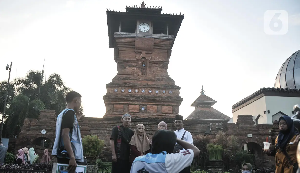 Fotografer saat memotret peziarah dengan latar belakang Menara Kudus, Kauman, Kabupaten Kudus, Jawa Tengah, Rabu (30/3/2022). Untuk sekali foto, fotografer membanderol harga Rp20 ribu, termasuk cetak. (merdeka.com/Iqbal S. Nugroho)