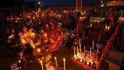 Kerabat menghabiskan malam di samping makam orang yang mereka cintai pada perayaan Hari Kematian di pemakaman Arocutin, Michoacan, Meksiko, 1 November 2021. Tradisi ini bertepatan dengan Hari Semua Orang Kudus dan Hari Semua Jiwa. (AP Photo/Eduardo Verdugo)