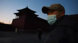 Seorang pria memakai masker pelindung di luar Kota Terlarang yang ditutup di Beijing pada Selasa (4/2/2020). Mencegah korban virus corona bertambah, China menutup  banyak destinasi wisata termasuk Kota Terlarang yang ditutup untuk kunjungan wisatawan sejak 24 Januari 2020 lalu. (GREG BAKER/AFP)