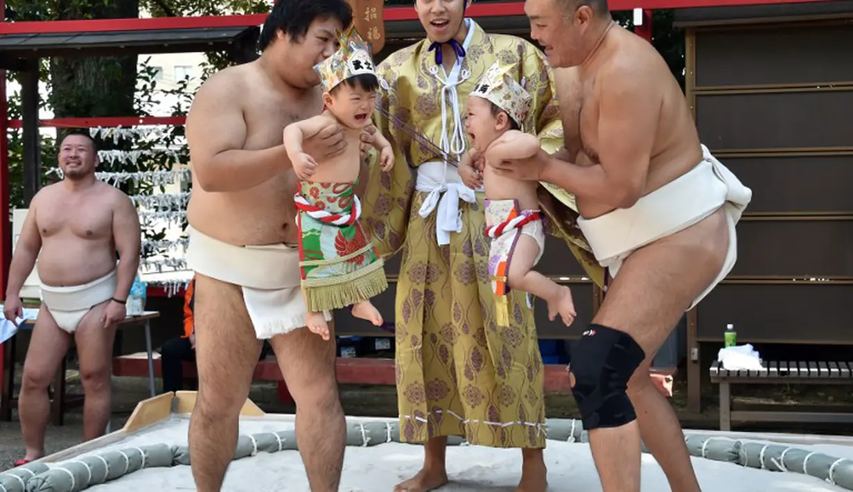 Selama "Lomba Bayi Menangis", para  pegulat sumo menggendong bayi di samping seorang wasit yang memakai kostum tradisional, Jepang, (21/9/14). (AFP PHOTO/ Yoshikazu TSUNO)