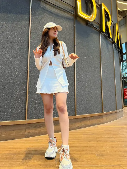 OOTD serba putih yang chic dari Sarah Keihl. Ia mengenakan atasan lengan panjang yang dikancingkan beberapa di bagian atas dan dibiarkan terbuka di bagian bawahnya, dipadu rok mini, topi, dan sneakers yang semuanya berwarna putih. [Foto: Instagram/sarahkeihl]