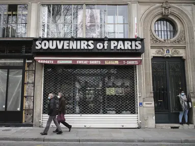 Orang-orang berjalan di depan toko suvenir yang tutup di Paris (22/3/2021).  Penduduk Paris dan beberapa wilayah Prancis lainnya menghabiskan akhir pekan pertama mereka di bawah penguncian terbatas selama sebulan.  (AP Photo/Lewis Joly)