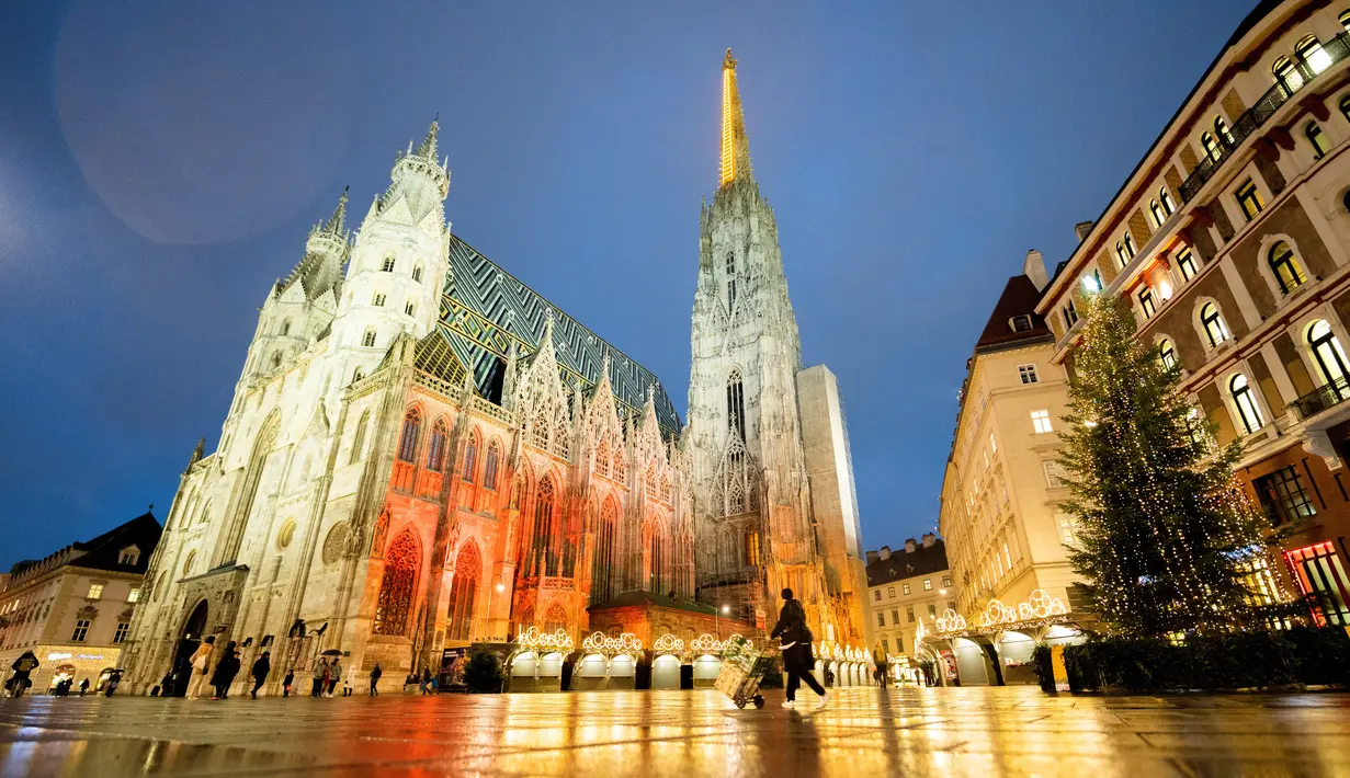 Orang-orang berjalan melewati Pasar Natal "Christkindlmarkt" Wina yang ditutup, dan Katedral St Stephen di Wina, Austria, Senin (22/11/2021). Austria kembali menerapkan lockdown penuh untuk mengekang infeksi Covid-19 menyebar ke seluruh Eropa. (GEORG HOCHMUTH / APA / AFP)