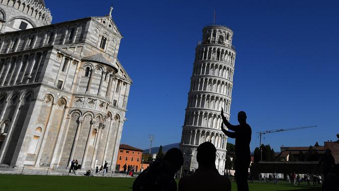 Turis berpose di depan Menara Pisa di kota Pisa, Italia pada 28 November 2018. Kemiringan Menara Pisa yang tersohor kini telah stabil setelah sedikit diluruskan dalam upaya menyelamatkan situs pariwisata ternama dunia itu. (Tiziana FABI / AFP)