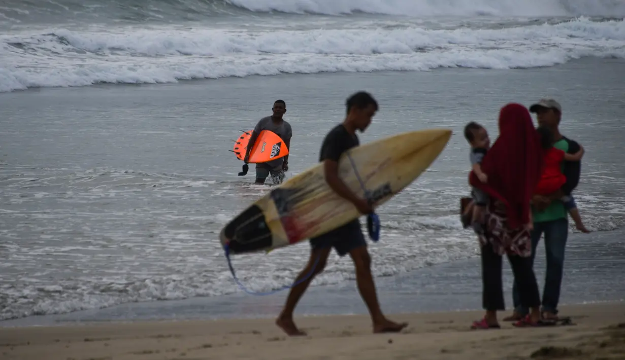 Peselancar memegang papan selancar saat berlibur Lebaran di Pantai Lhoknga, Aceh Besar, Aceh, Minggu (9/6/2019). (CHAIDEER MAHYUDDIN/AFP)