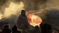 Seorang pengunjuk rasa berdiri di barikade ketika truk terus memblokir pusat kota sebagai protes atas pembatasan COVID-19, di Ottawa, Ontario, Sabtu, 5 Februari 2022. (Adrian Wyld/The Canadian Press via AP)