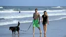 Pasangan membawa seekor anjing berjalan di Jacksonville Beach, Florida (17/4/2020). Pantai dibuka hanya untuk jam terbatas dan hanya bisa digunakan untuk berenang, berlari, berselancar, berjalan, bersepeda, memancing, dan merawat binatang peliharaan. (Sam Greenwood / Getty Images / AFP)