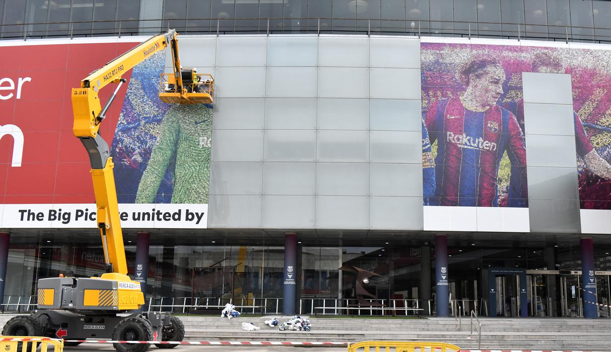 Pekerja menghapus poster yang menampilkan pemain depan Barcelona asal Argentina Lionel Messi di stadion Camp Nou di Barcelona (10/8/2021). Para pendukung PSG berharap untuk melihat pemain asal Argentina itu bergabung ke klub milik Qatar setelah hengkang dari Barcelona. (AFP/ Pau Barrena)