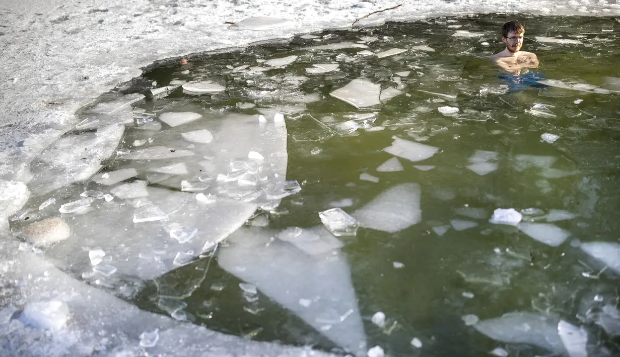 Seorang pria mandi di lubang es di danau dekat Vilnius, Lithuania, Minggu (13/2/2022). Suhu udara 0 derajat Celcius (32 derajat Fahrenheit). (AP Photo/Mindaugas Kulbis)